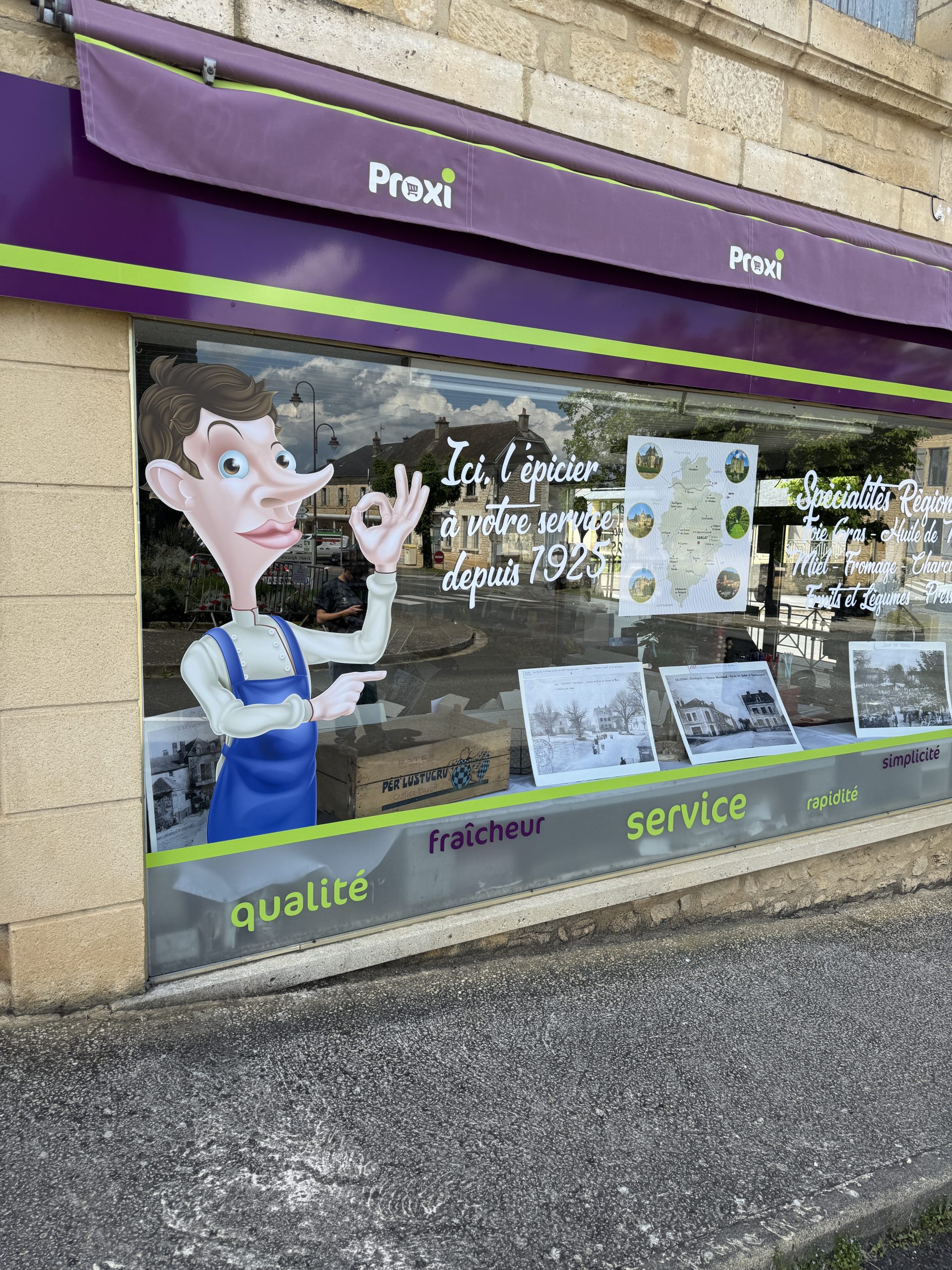 Vitrine de l’épicerie Proxi de Salignac habillée par Avenir Impressions : lettrage blanc découpé, personnage de l’épicier et bandeau bas