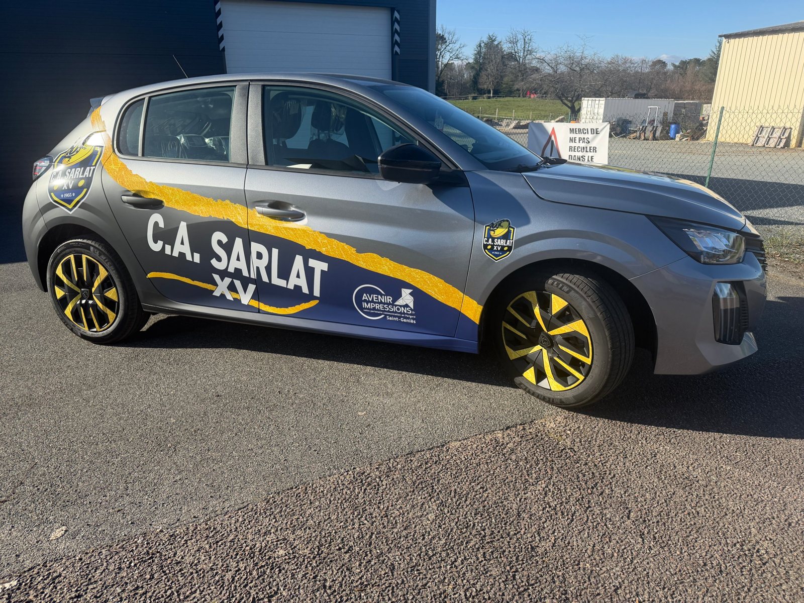 Peugeot 208 du CA Sarlat Rugby de profil : covering bleu marine, noir mat et coup de pinceau doré, blason du club