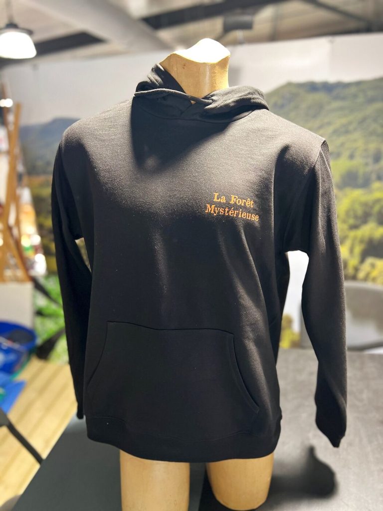 Face du sweat à capuche noir avec « La Forêt Mystérieuse » imprimé en orange côté cœur