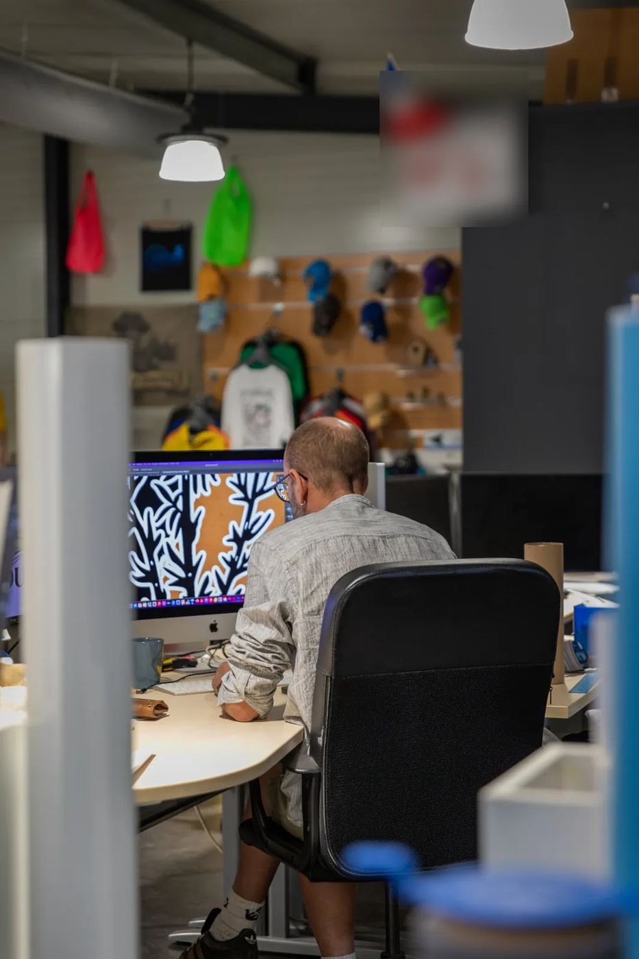 Gaëtan dessine un visuel au studio de création, devant le mur de textiles personnalisés