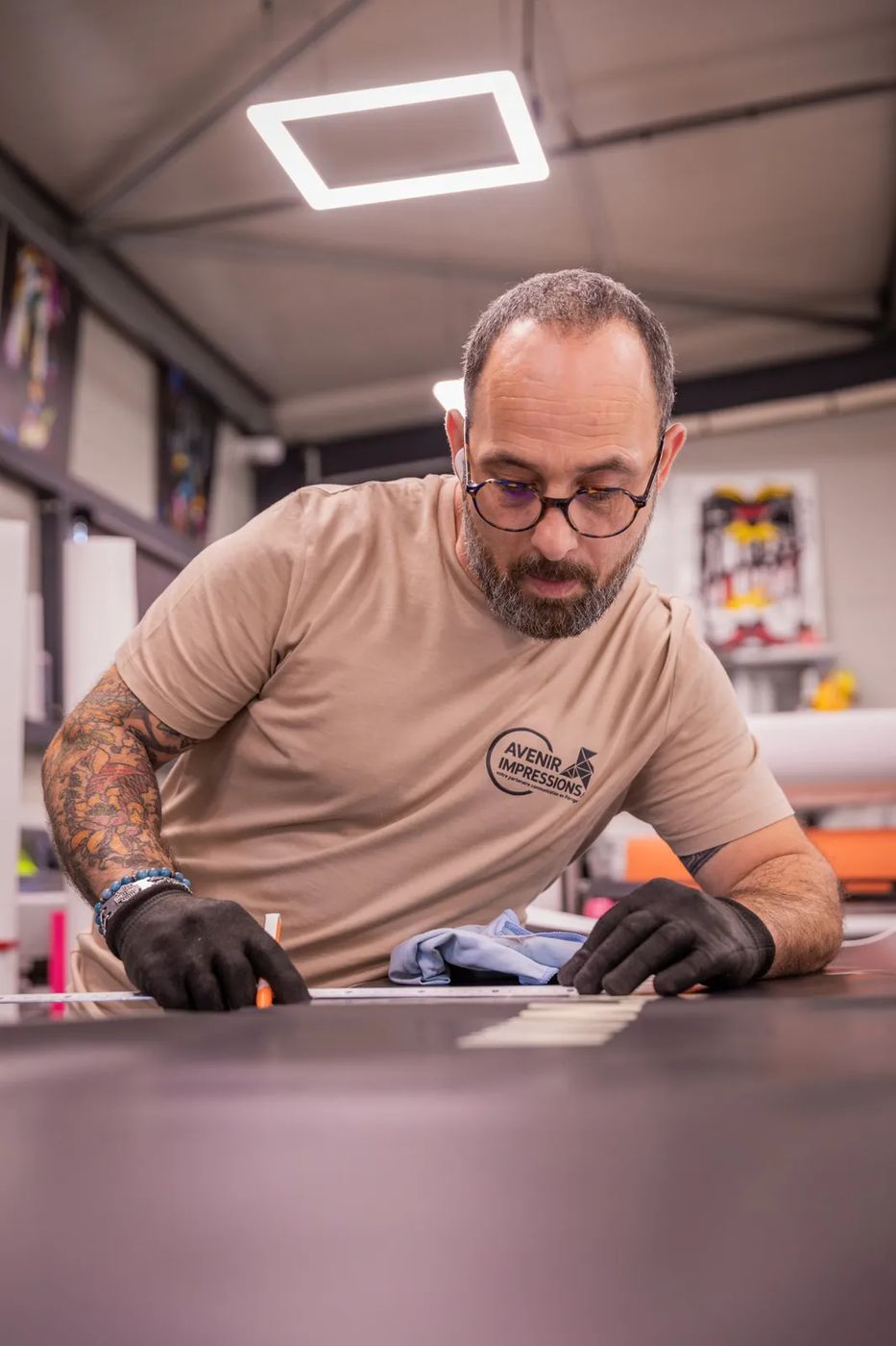 Mickey découpe un film adhésif à la règle sur la table de l’atelier