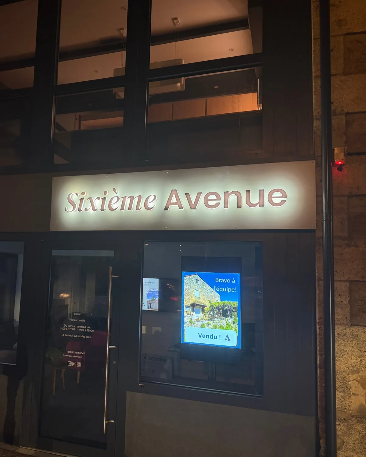Enseigne lumineuse Sixième Avenue en lettres rétroéclairées sur la façade de l’agence immobilière à Sarlat, la nuit